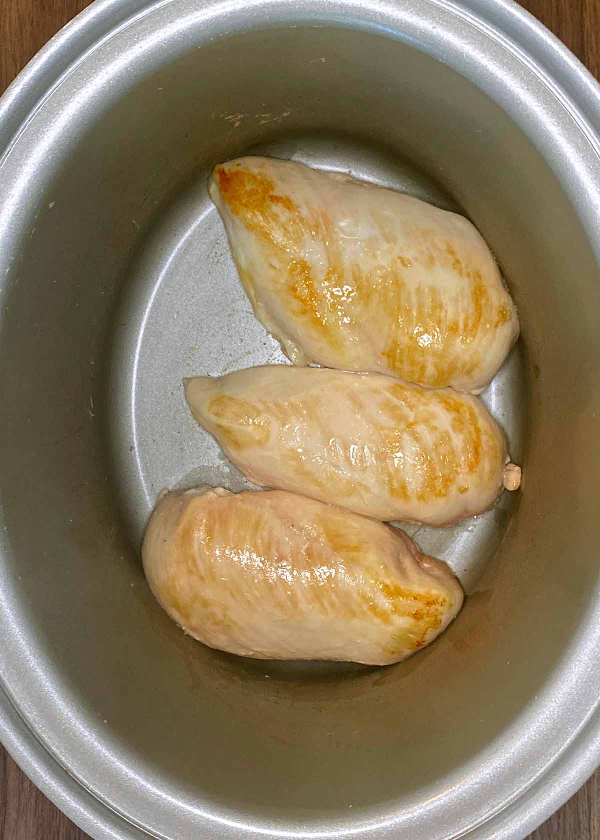 Three cooked chicken breasts in a slow cooker pot.