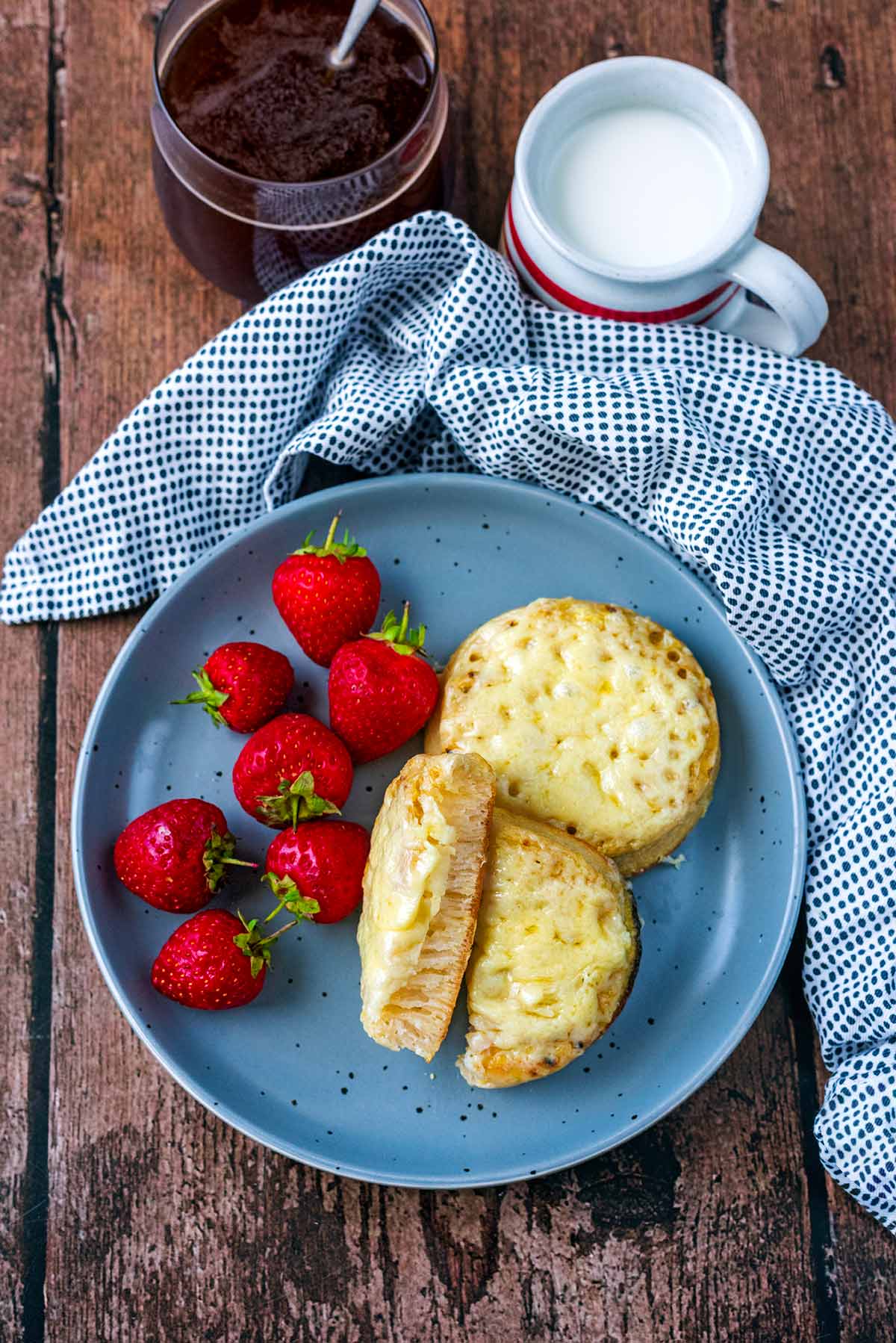Two cheesy crumpets on a plate with some strawberries.