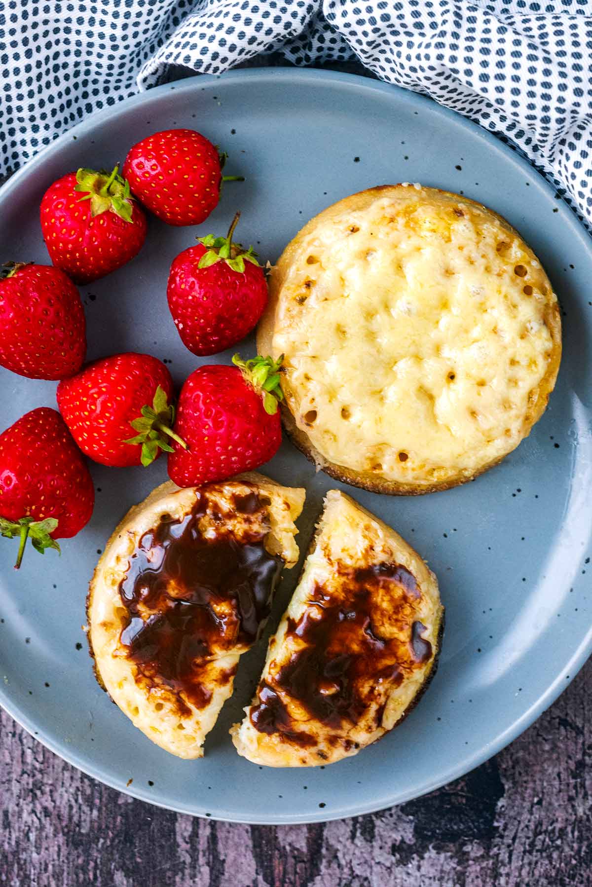Two cheesy crumpets on a plate, one has marmite spread on it.
