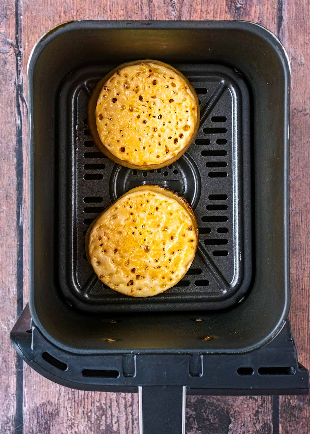 Two egg soaked crumpets in an air fryer basket.