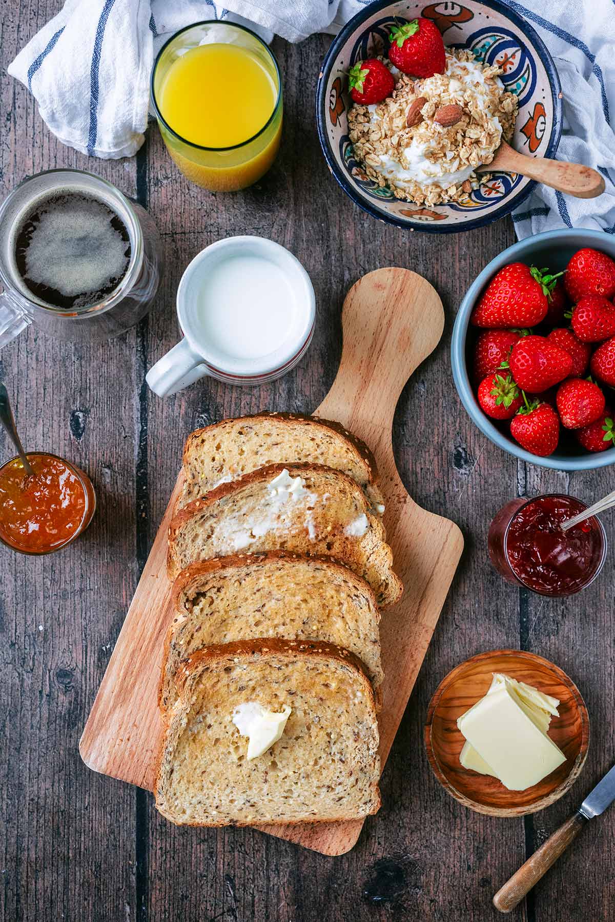Four slices of buttered toast next to bowls of granola, berries and a cup of coffee.