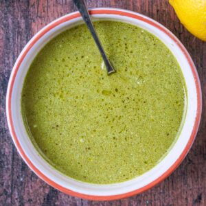 A bowl of pesto salad dressing with a spoon in it.