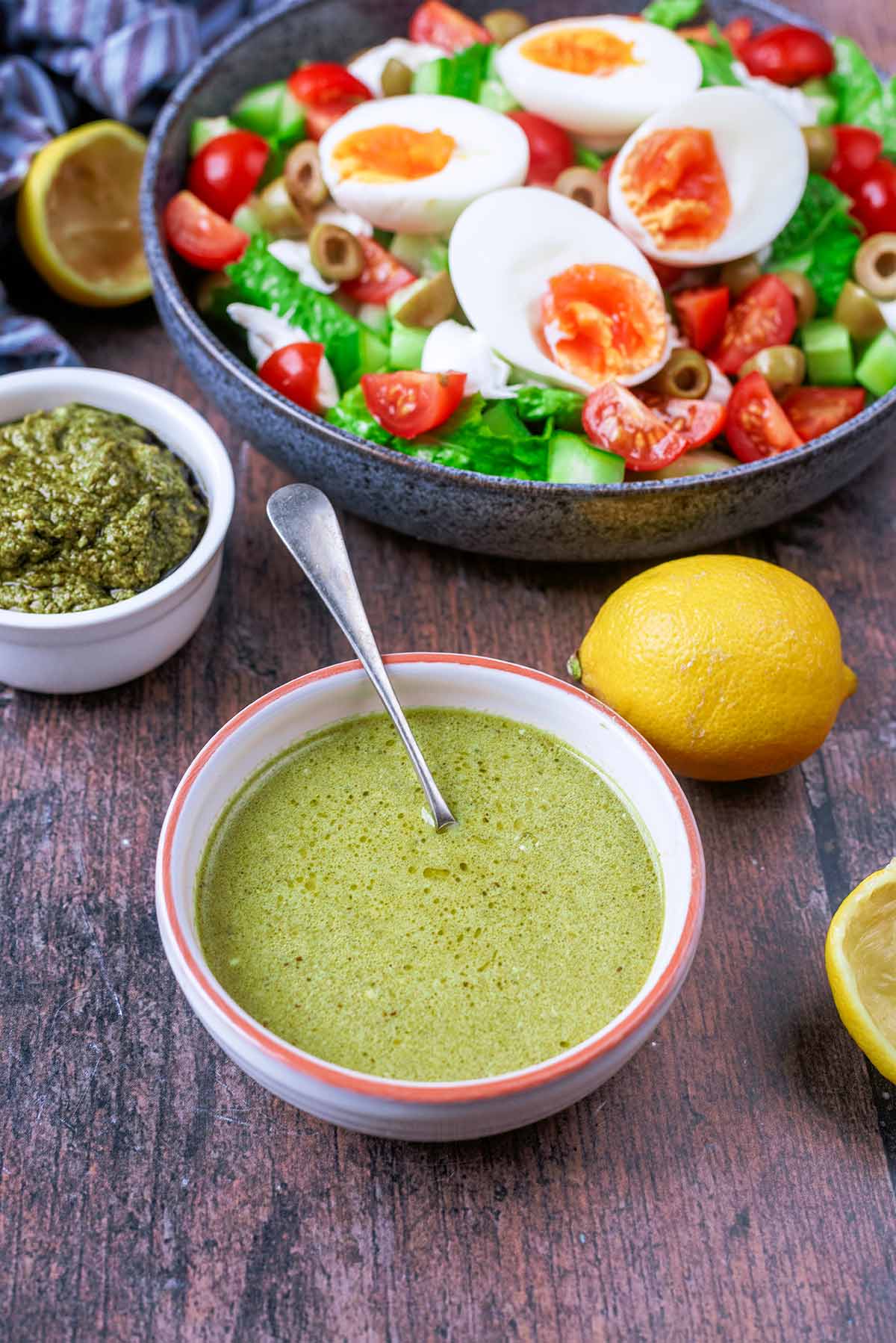 A bowl of green pesto dressing in front of a bowl of egg salad.
