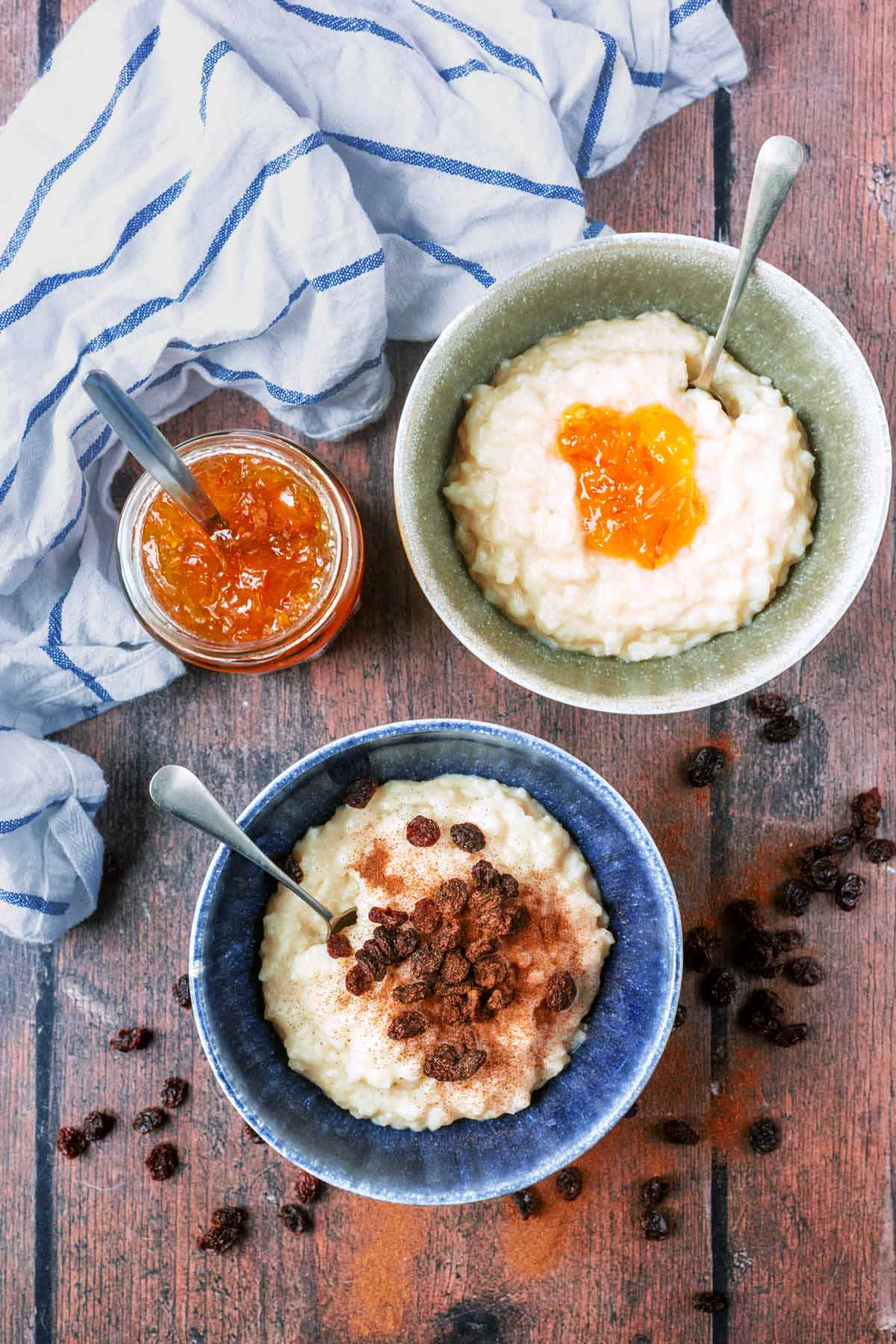 Two bowls of rice pudding, one topped with marmalade, one topped with raisins.