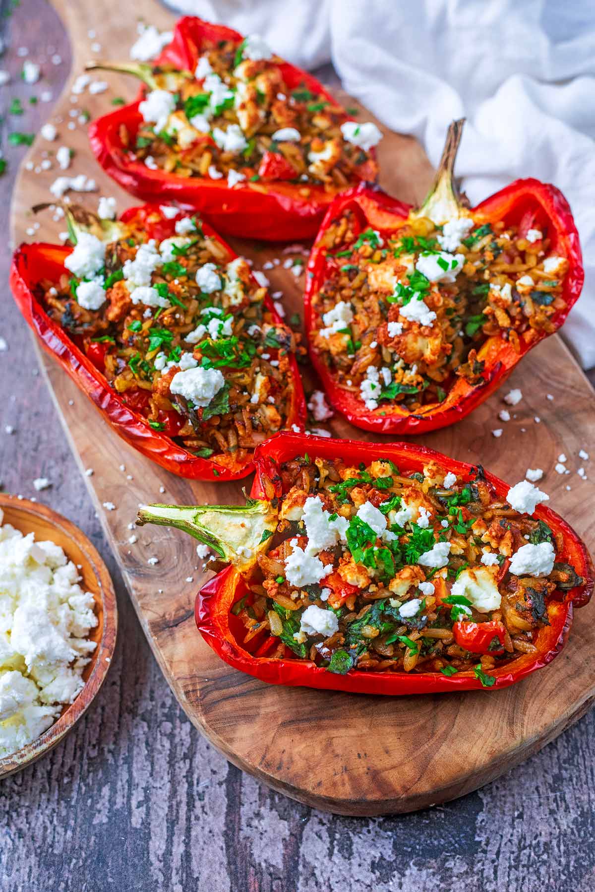 Stuffed red pepper halves on a board next to a small bowl of feta cheese.