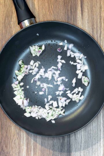 Chopped shallots and crushed garlic frying in a pan.