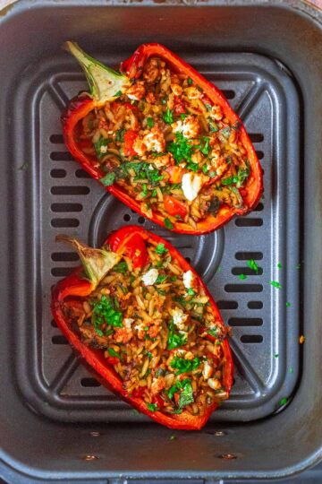 Cooked stuffed peppers in an air fryer basket.