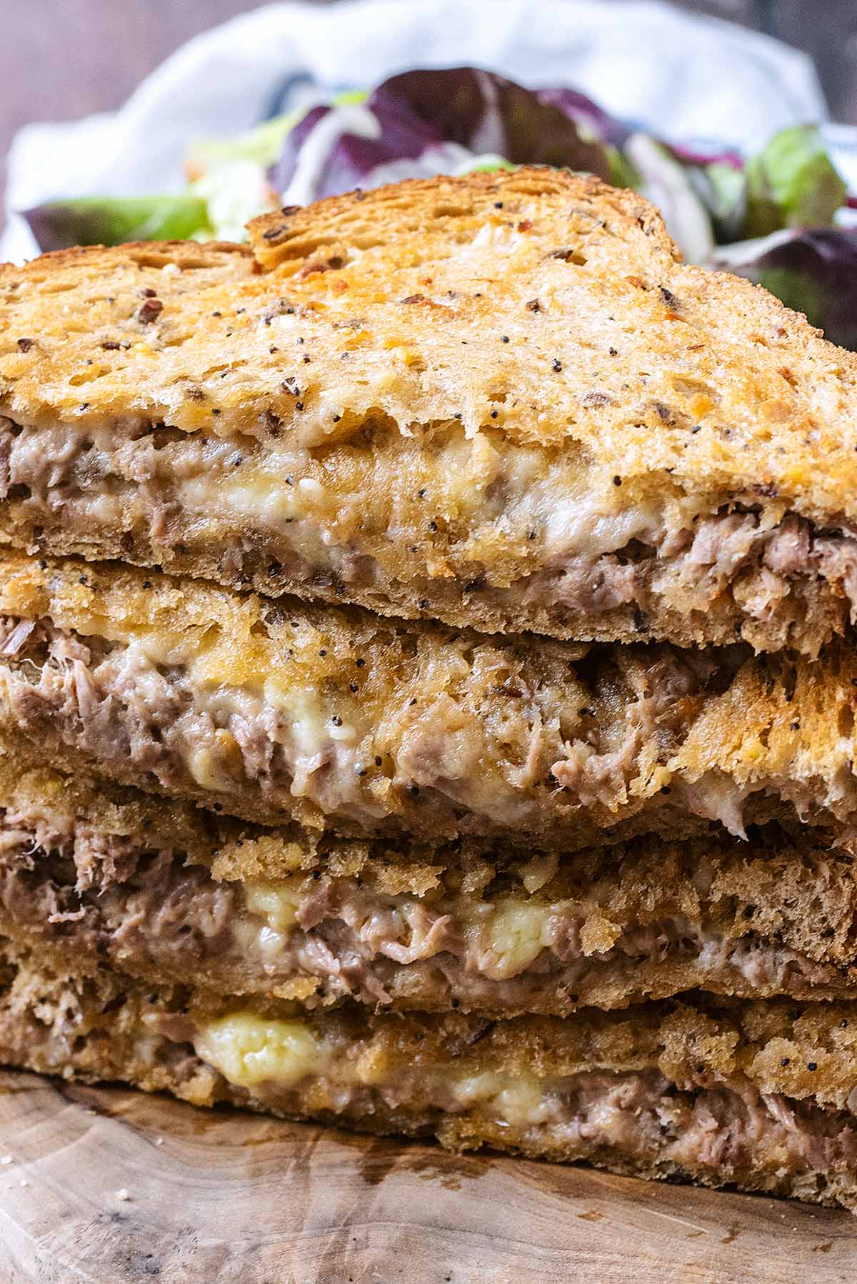 Four triangular toasted tuna sandwiches piled up on top of each other.