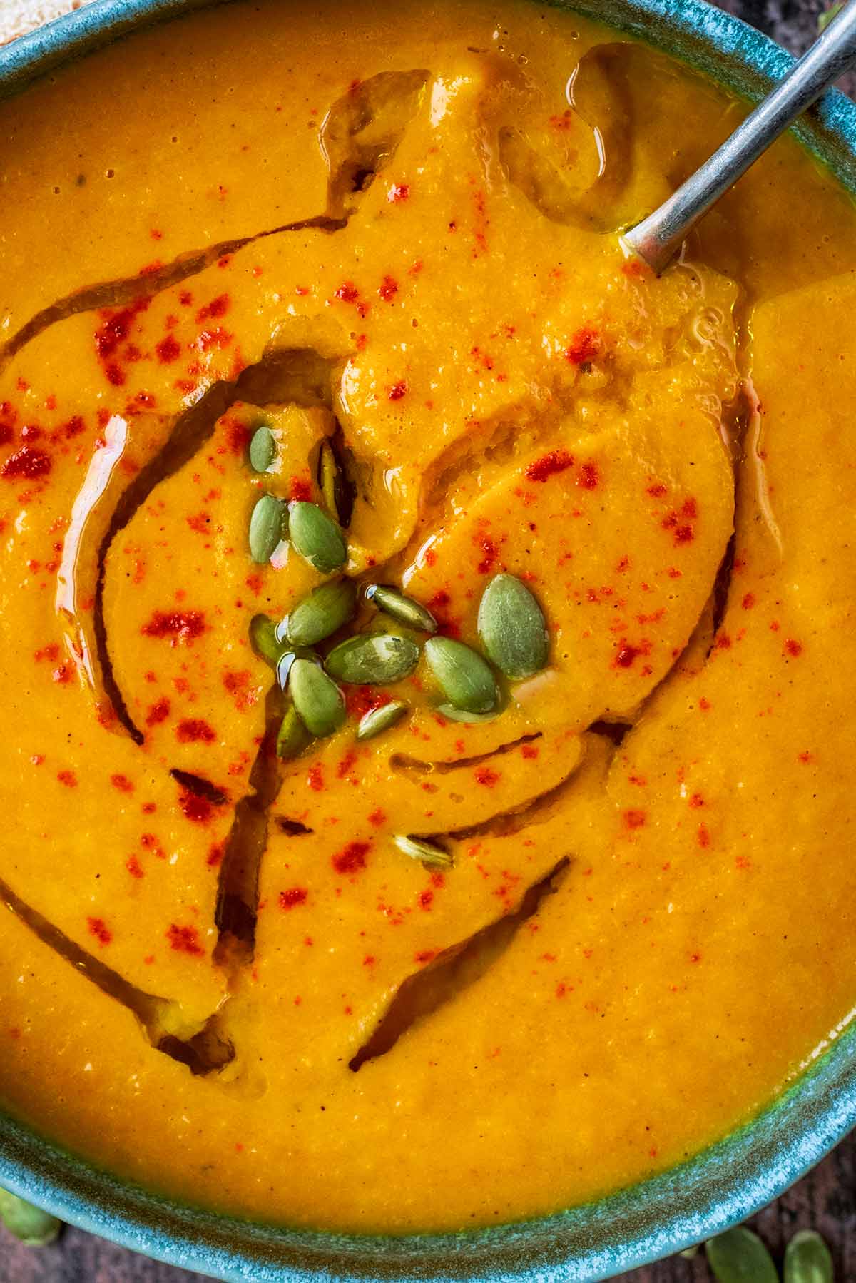 Pumpkin seeds and a drizzle of oil on top of a bowl of orange coloured soup.