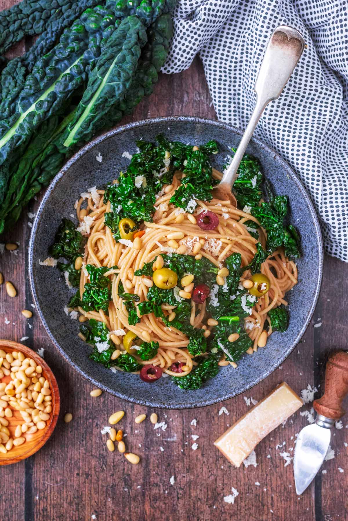 A bowl of spaghetti mixed with cooked cavolo nero on a wooden surface.