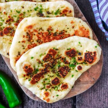 Chilli naan breads on a wooden serving board.