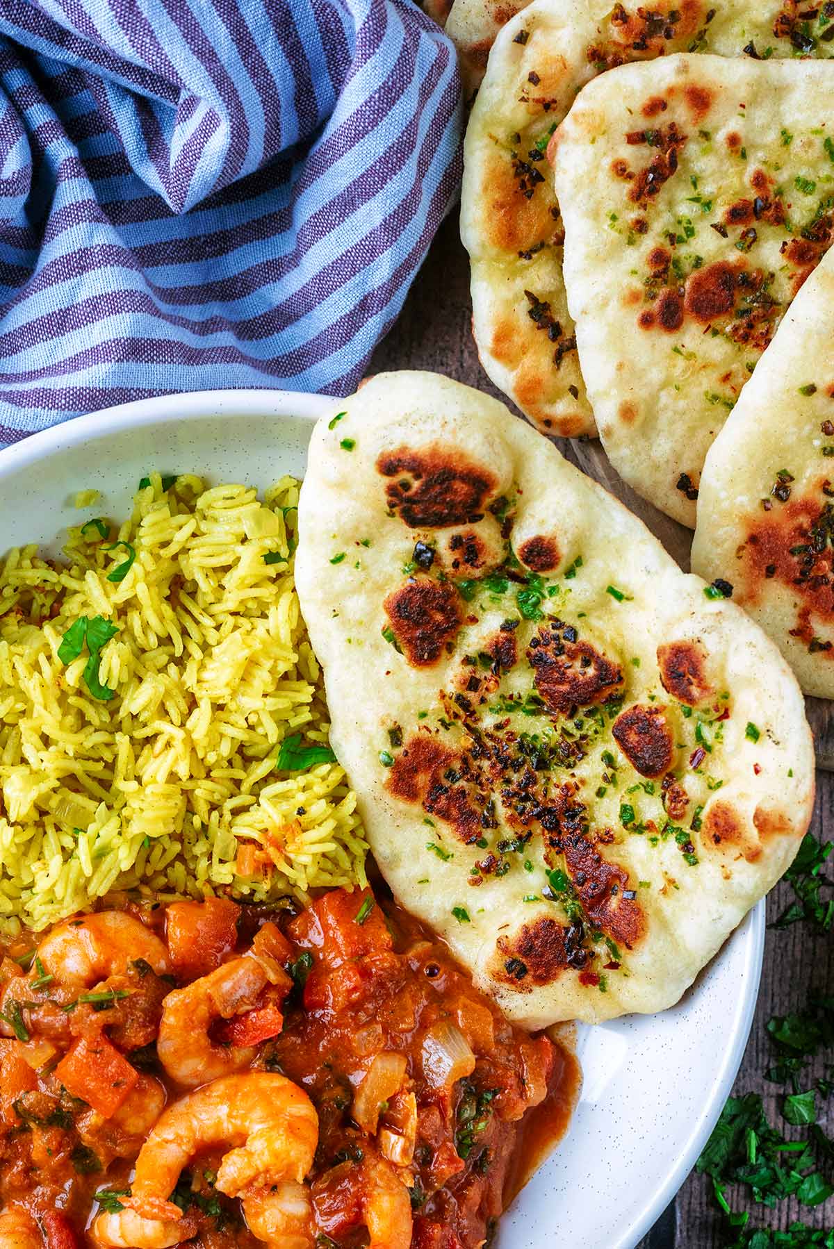 A naan bread sat on the side of a bowl of prawn curry and rice.
