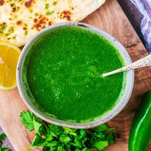 A bowl of coriander chutney with a small spoon in it.