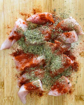Chunks of chicken on a wooden board coated in herbs and spices.