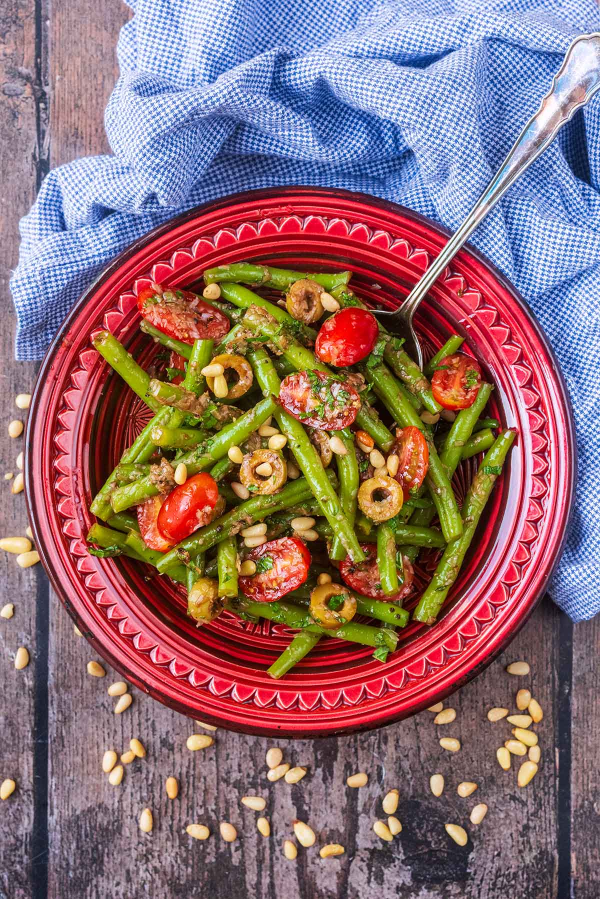 A red bowl full of green beans and cherry tomatoes covered in a dressing.