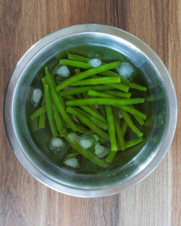 Cooked green beans in a bowl of iced water.