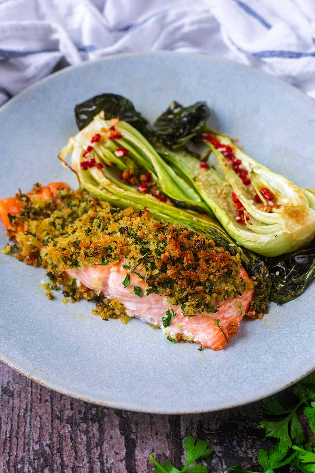A crusted salmon fillet on a plate with some cooked pak choi.