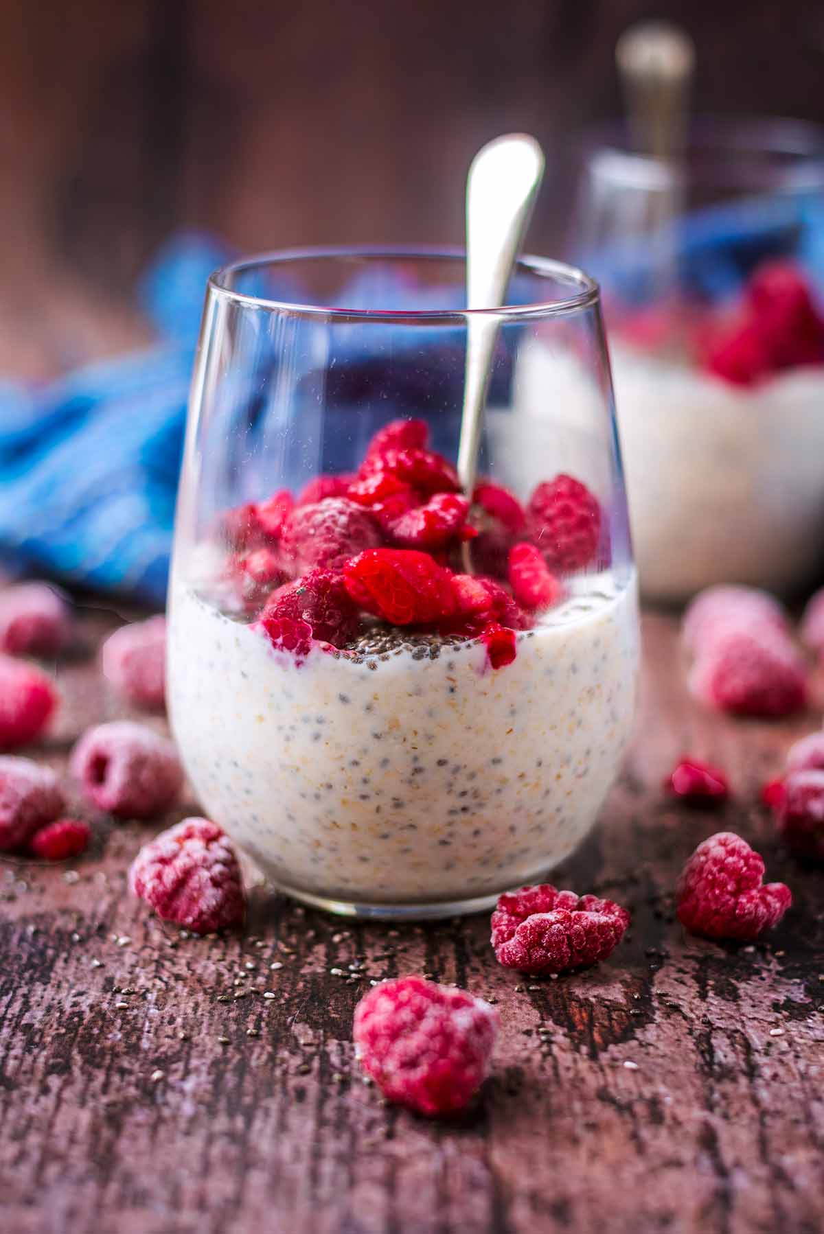 A glass of overnight oats topped with raspberries and surrounded by more raspberries.