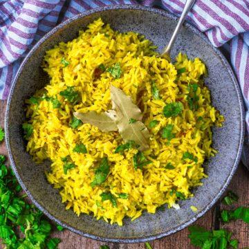 A bowl of yellow pilau rice with a spoon in it.