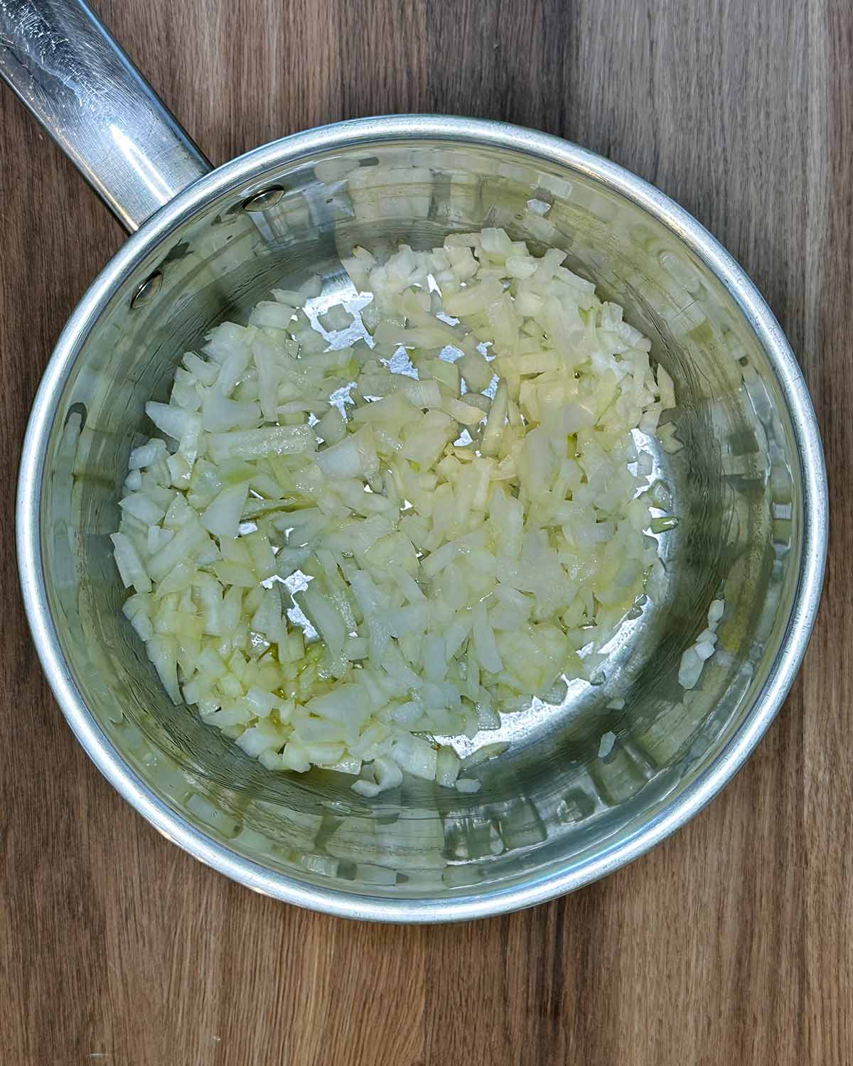 Chopped onion cooking in a silver saucepan.