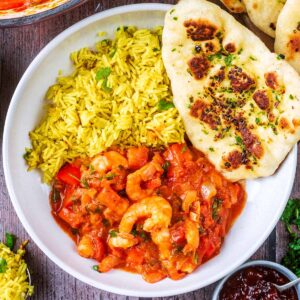 Prawn tikka masala in a bowl with rice and a naan bread.