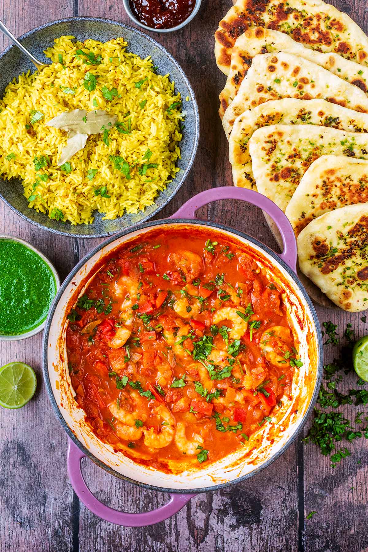 A large pan full of a prawn curry next to rice and naan breads.