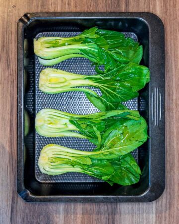 Half heads of pak choi, brushed with oil, in a roasting pan.