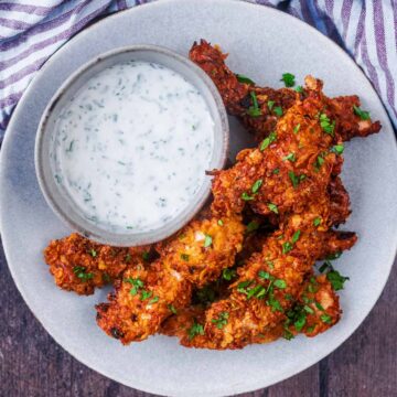 Air fryer chicken tenders on a plate with a bowl of creamy dip.