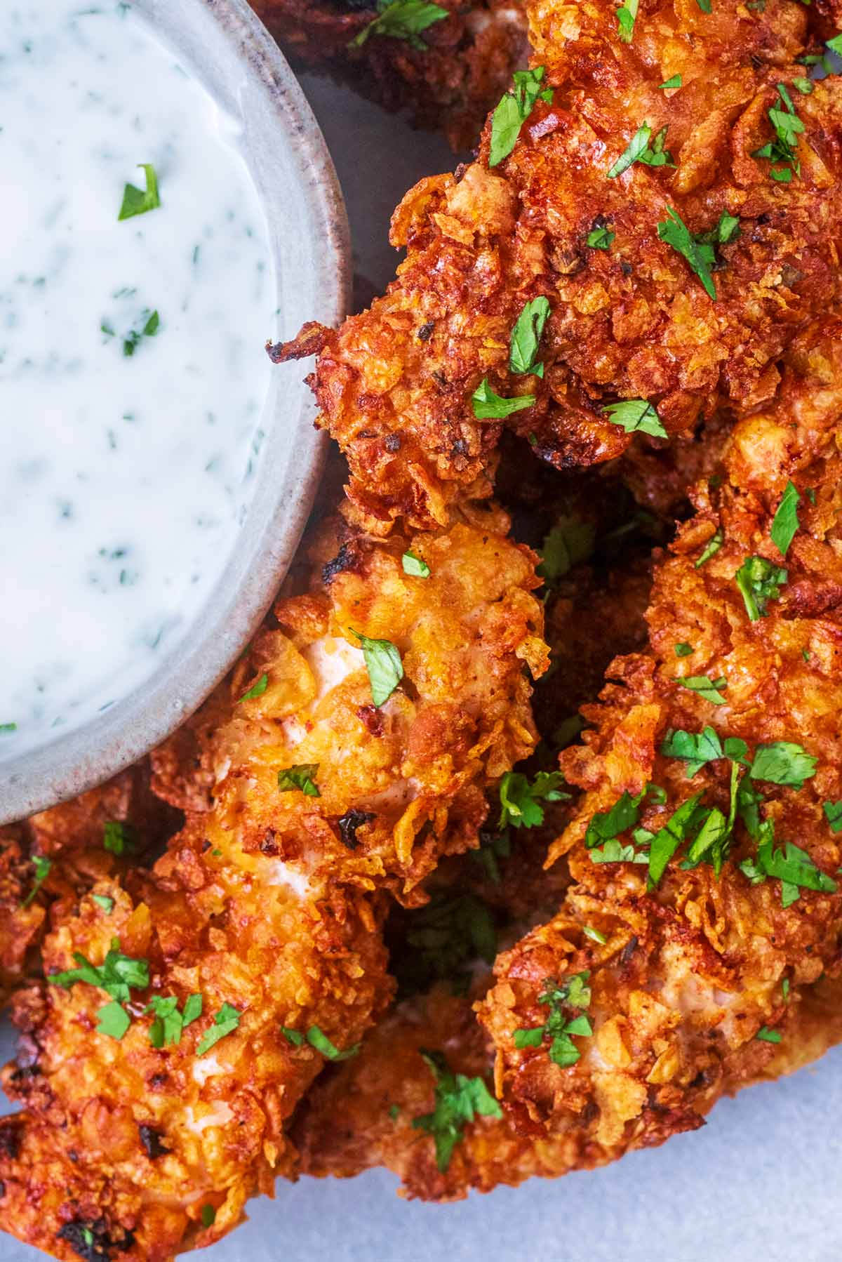 Cornflake coated chicken tenders with chopped herbs sprinkled over them.