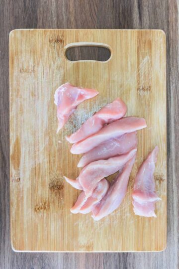 A chopping board with sliced chicken breast on it.