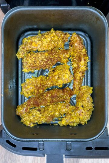 Uncooked coated chicken tenders in an air fryer basket.