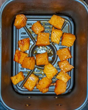 The coated salmon chunks in an air fryer basket.