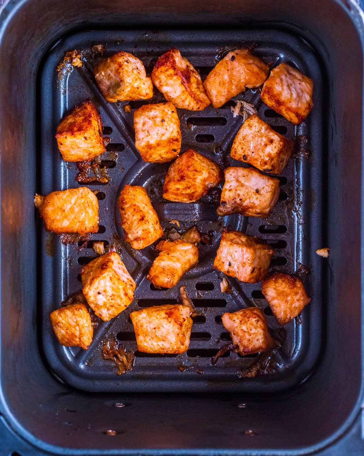 Cooked salmon chunks in an air fryer basket.