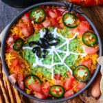 A bowl of halloween dip decorated with a sour cream spider web.