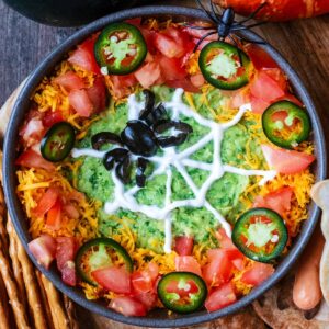 A bowl of halloween dip decorated with a sour cream spider web.