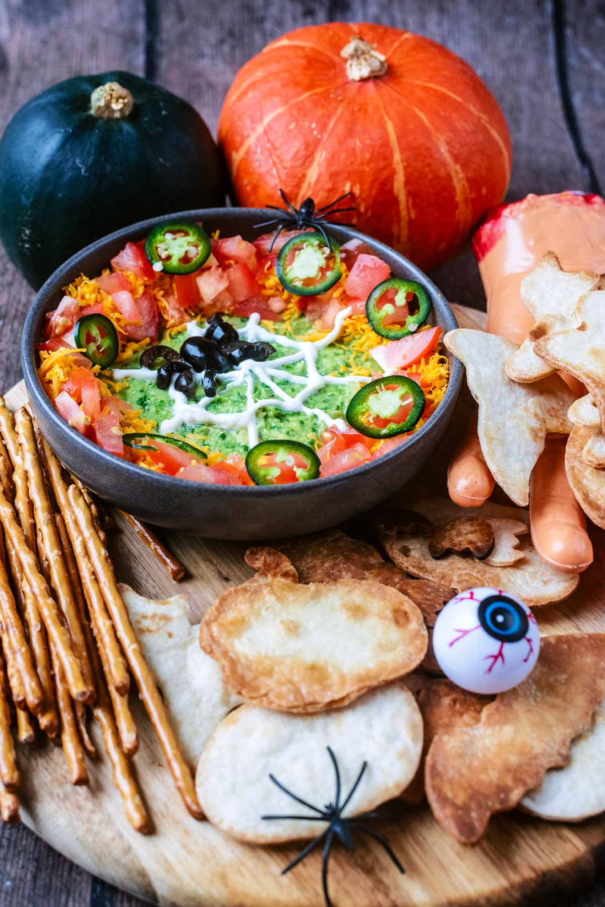 A halloween inspired dip on a wooden board with Halloween shaped tortilla chips.