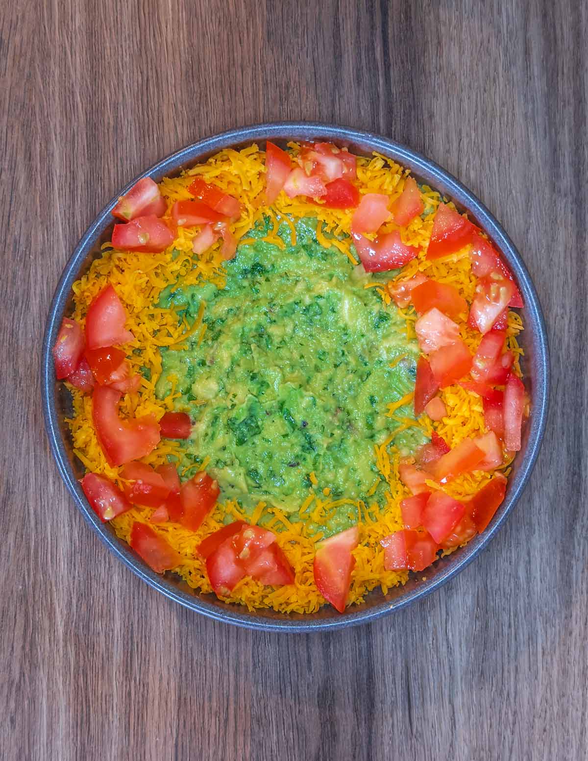 Grated cheese and chopped tomatoes put around the edge of the guacamole.