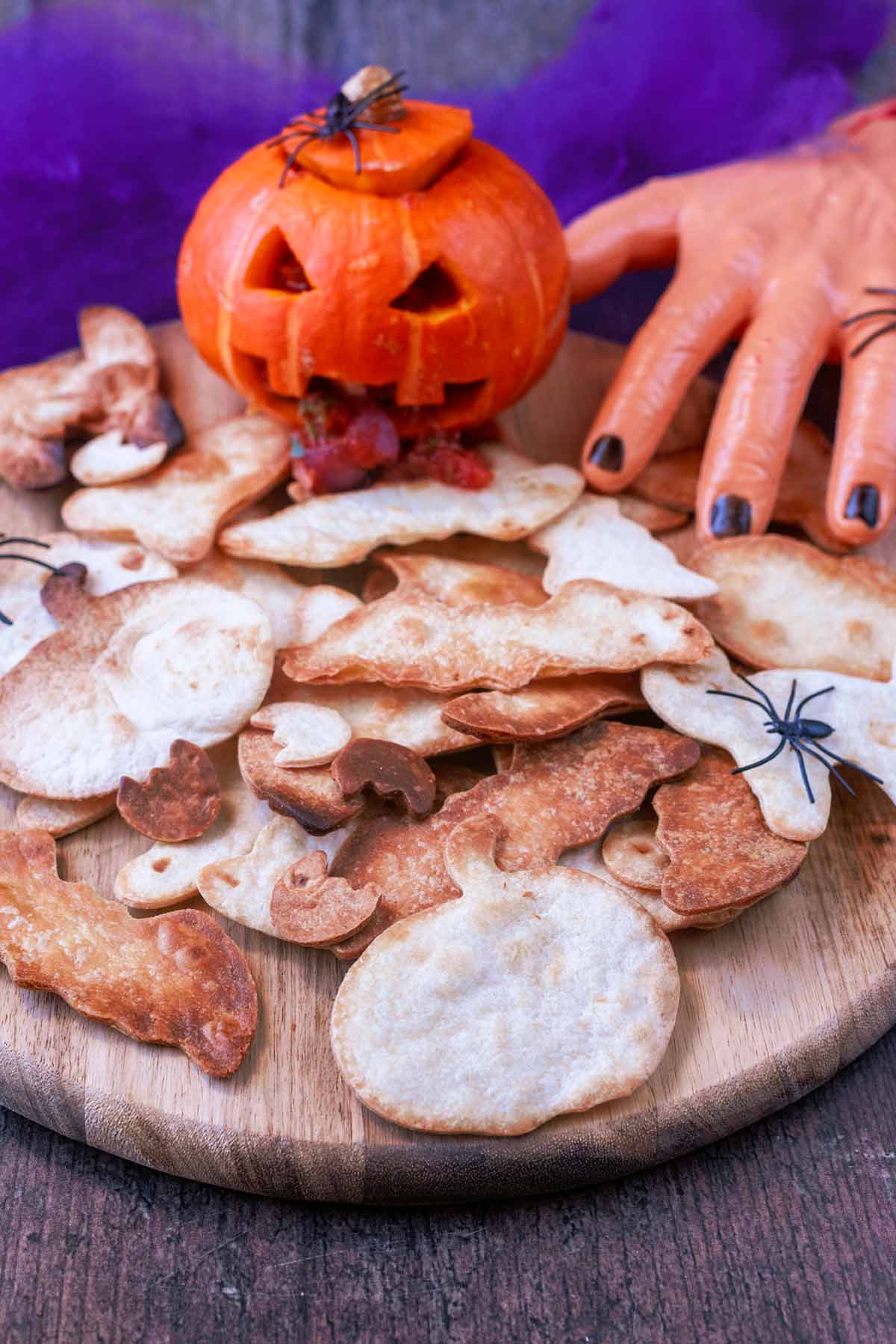 A wooden board covered in halloween shaped tortilla chips with a pumpkin.