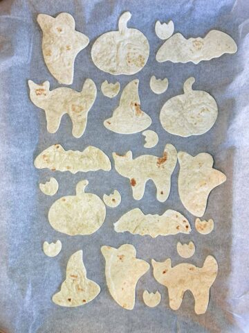A lined baking tray with halloween shaped tortilla cutouts on it.