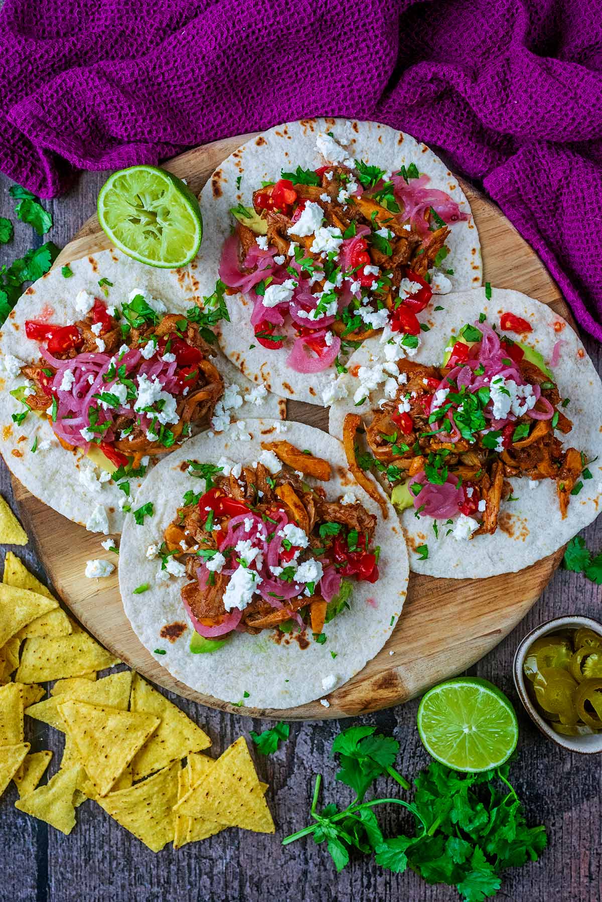 Four tacos laid out on a round wooden serving board.