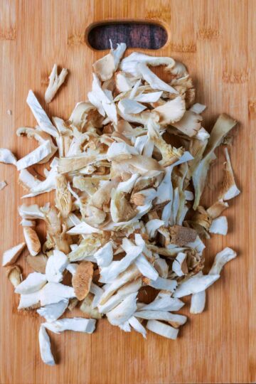 Mushrooms torn into strips on a wooden chopping board.
