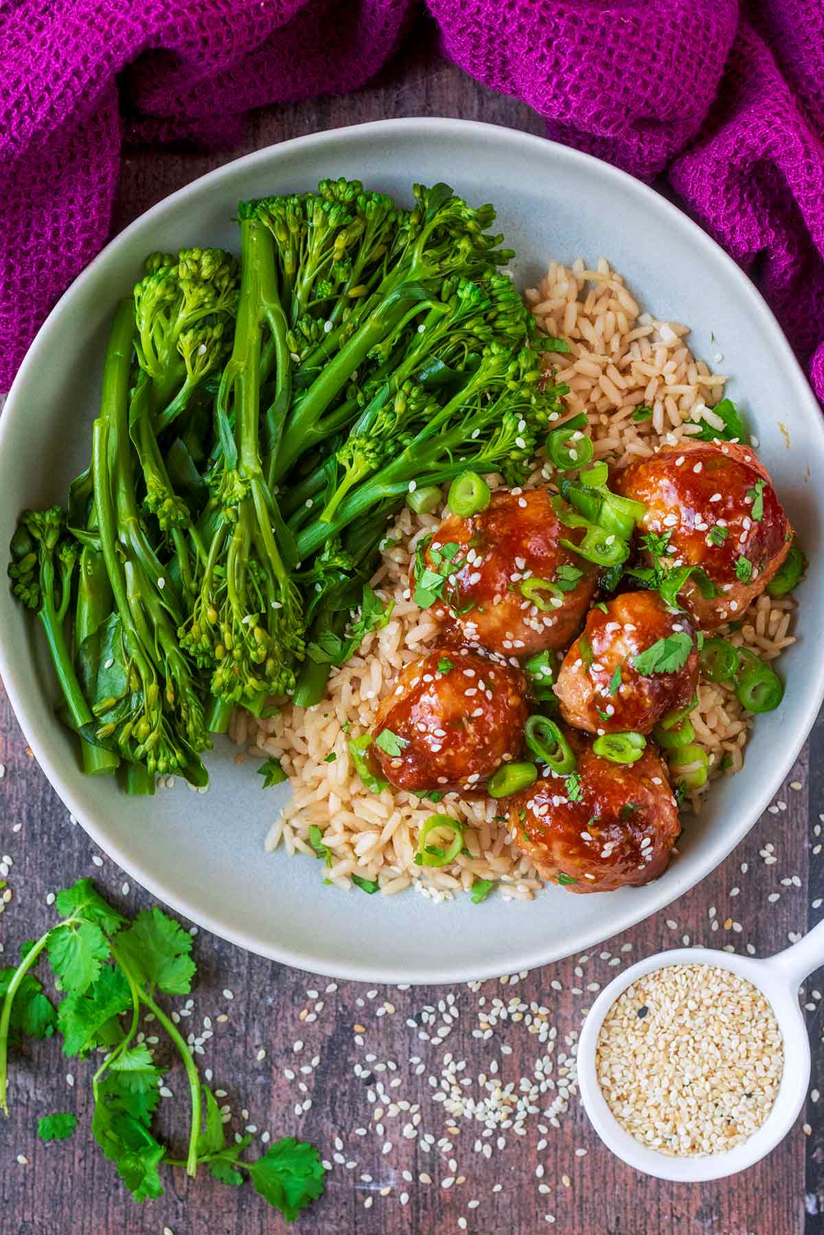 A plate of meatballs in sauce with rice and broccoli.