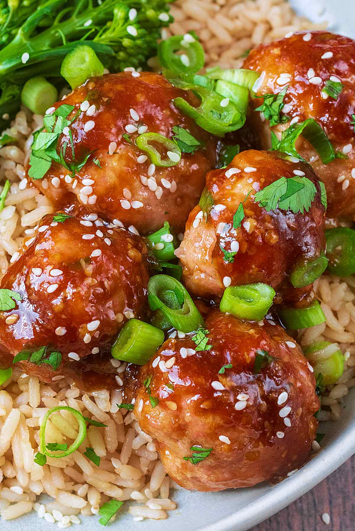 Cooked chicken meatballs coated in sauce topped with spring onions and sesame seeds.