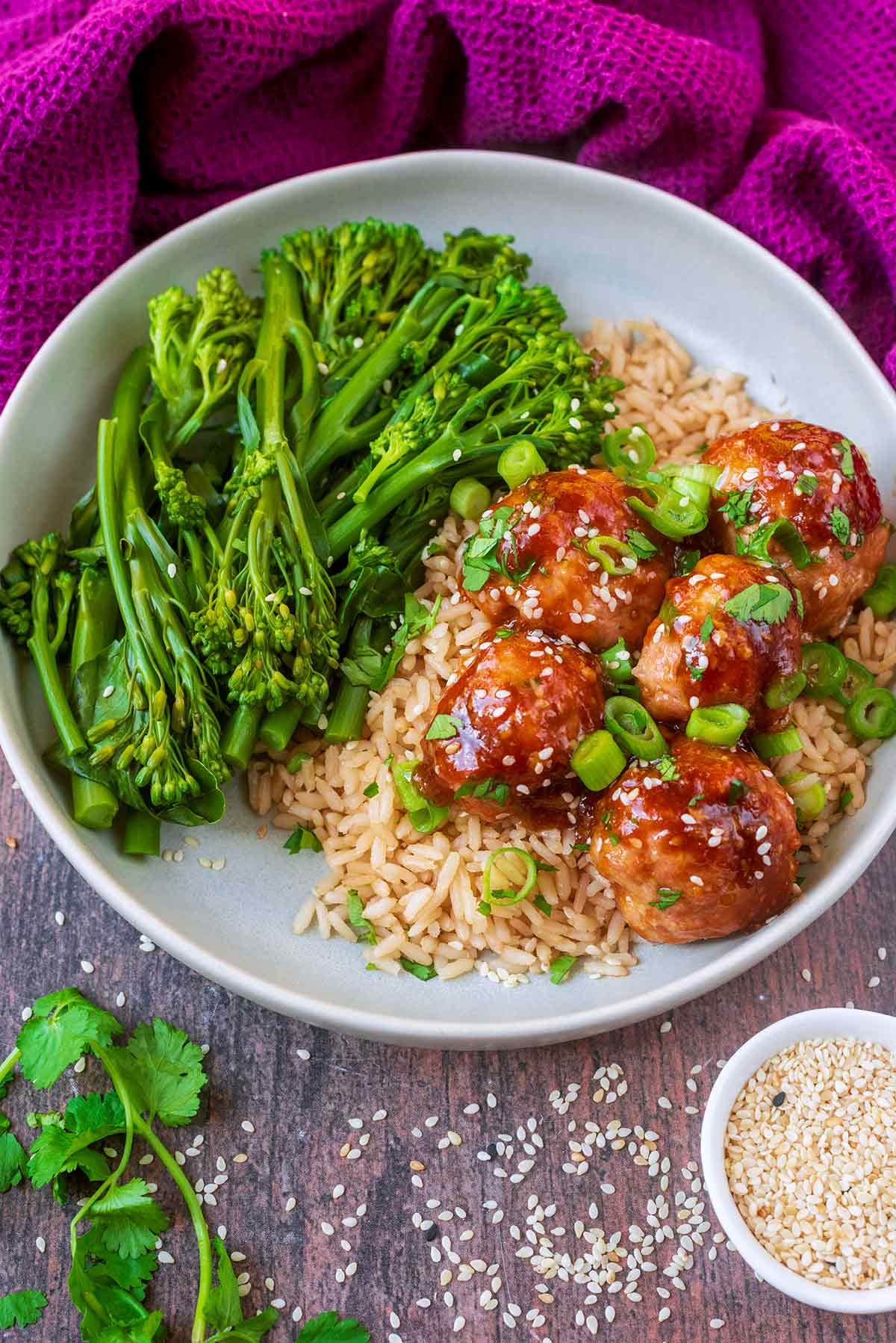 A plate of meatballs, rice and broccoli in front of a purple towel.