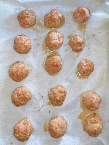 Fifteen cooked chicken meatballs on a lined baking tray.