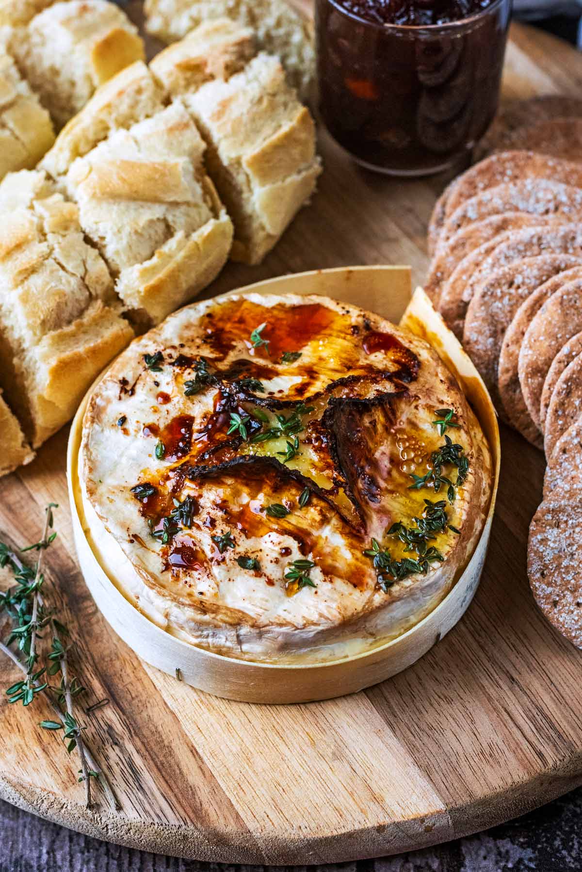 A round of baked Camembert on a board with slices of crusty bread and some crackers.