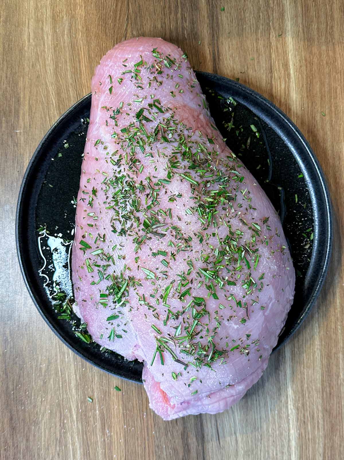 A raw turkey breast covered in oil, salt and herbs.