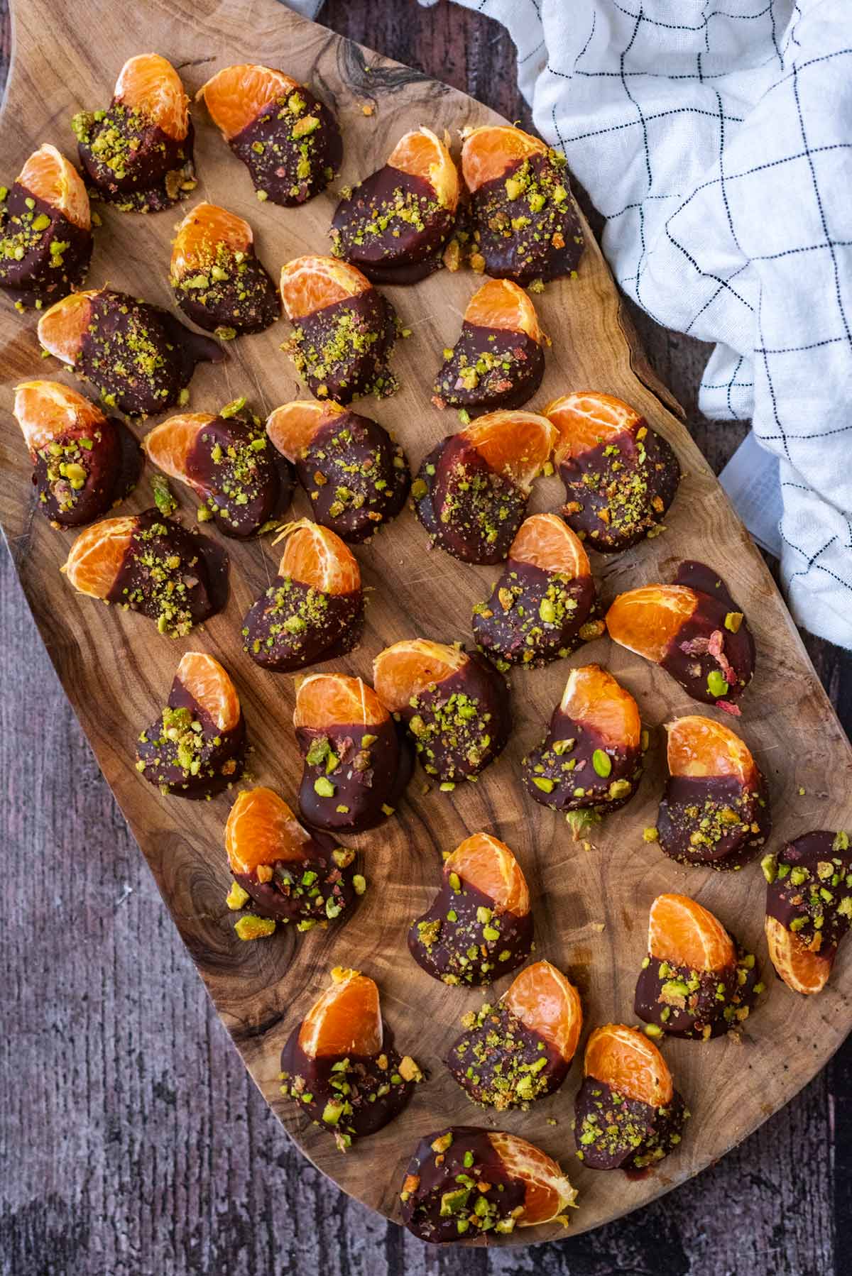 Thirty one satsuma segments, half dipped in chocolate all on a wooden board.
