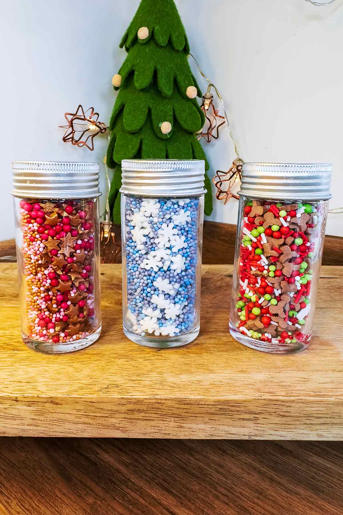 Three jars of sugar sprinkles in front of a small felt Christmas tree.