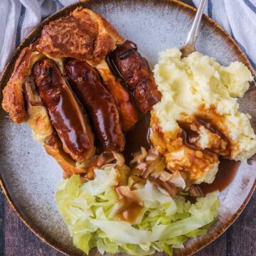 A portion of toad in the hole on a plate with mashed potato and cabbage.